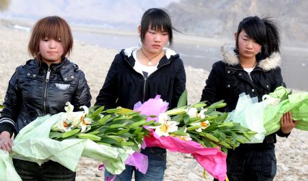 Photo taken on March 14, 2009 shows three employees of the Yishion garment store present fresh flowers by the Lhasa river to mourn the five sales assistants burned to death in an arson attack by rioters on March 14, 2008 in Lhasa, capital of southwest China's Tibet Autonomous Region. (Xinhua/Soinam Norbu)