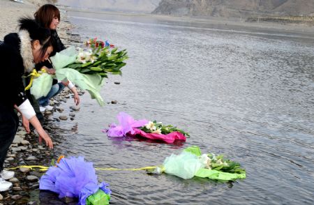 Photo taken on March 14, 2009 shows employees of the Yishion garment store put bunches of fresh flowers into the Lhasa river to mourn the five sales assistants burned to death in an arson attack by the rioters on March 14, 2008, in Lhasa, capital of southwest China's Tibet Autonomous Region. (Xinhua/Soinam Norbu)